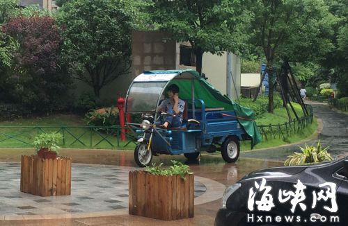 這名快遞哥騎行在小區(qū)通道內(nèi)，一邊接打手機(jī)，一邊還把腳架在車前欄桿上